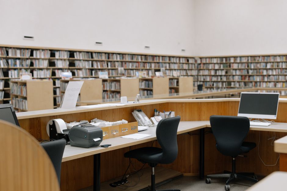 Interior view of a university library with bookshelves and computer workstations.